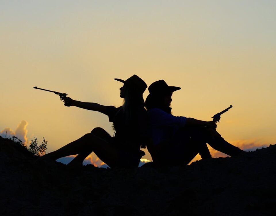 A influência das armas no bem-estar mental: mito ou realidade? Silhouette of Two People Holding Revolver Pistols Sitting on Hill
