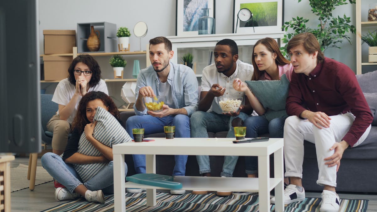 Assistir filmes de terror pode melhorar seu humor, você sabia? A group of people sitting on a couch watching tv