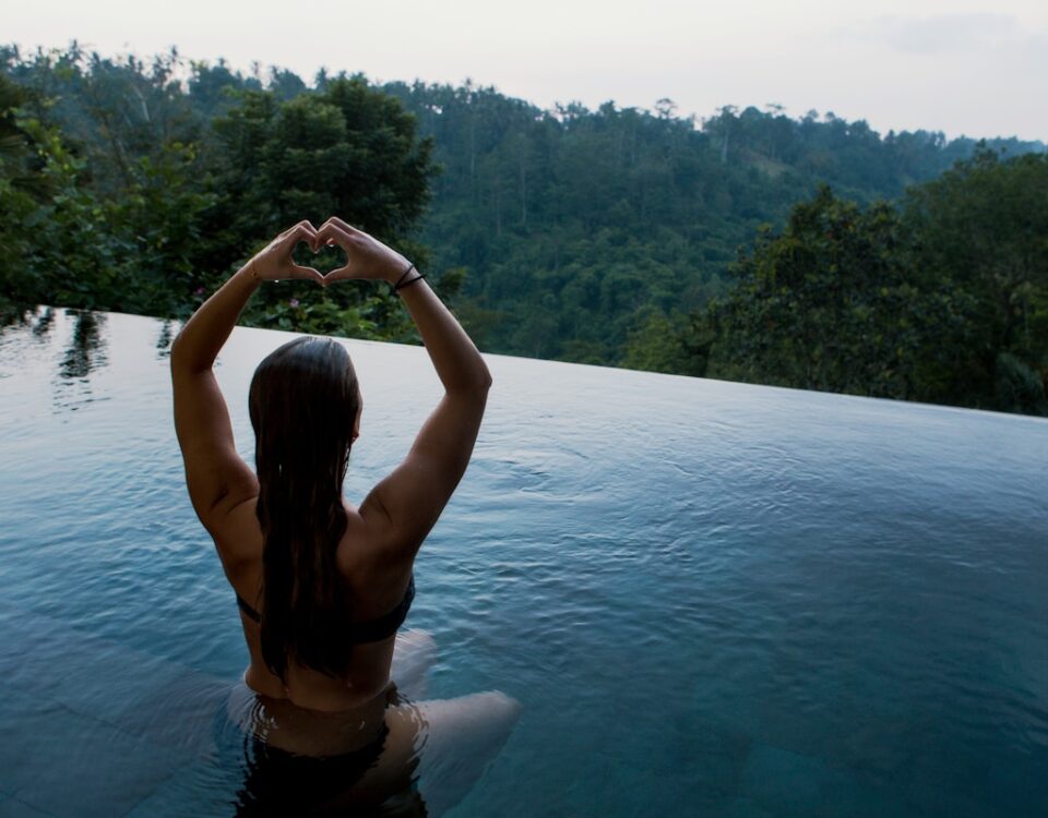 Estoicismo e bem-estar: viver melhor com menos preocupações woman in infinity pool making heart hand gesture facing green leafed trees