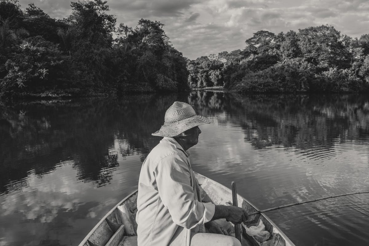 An elderly man peacefully fishing on a calm, reflective lake in black and white.
