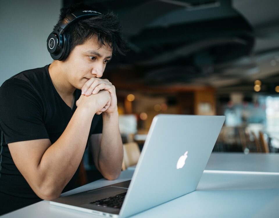 man wearing headphones while sitting on chair in front of MacBook