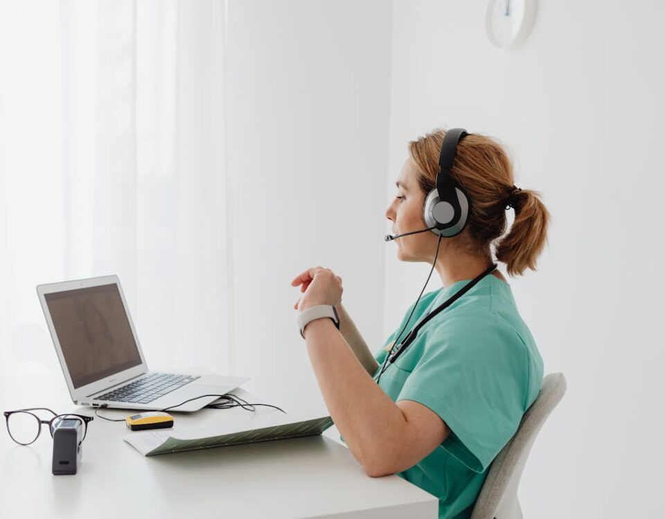 Vantagens práticas dos robôs no atendimento digital A female doctor using a laptop for an online consultation, wearing a headset in a bright office.