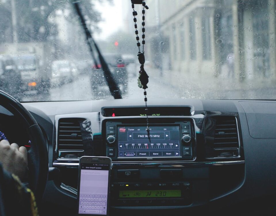 Cuidados essenciais para dirigir com mais segurança Car interior with driver navigating rainy cityscape using phone and dashboard.