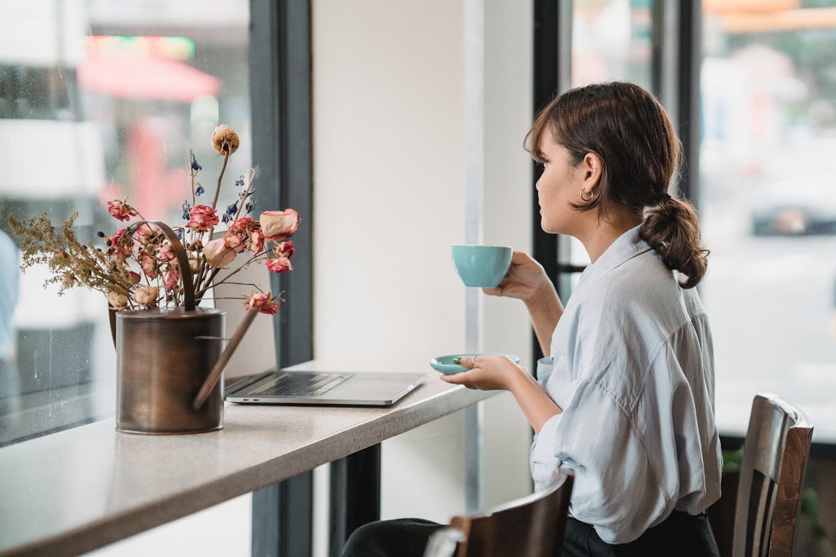 Como manter o equilíbrio na rotina de auxiliar administrativo Elegant woman sipping coffee by the window in a cozy café, enjoying the peaceful ambiance.