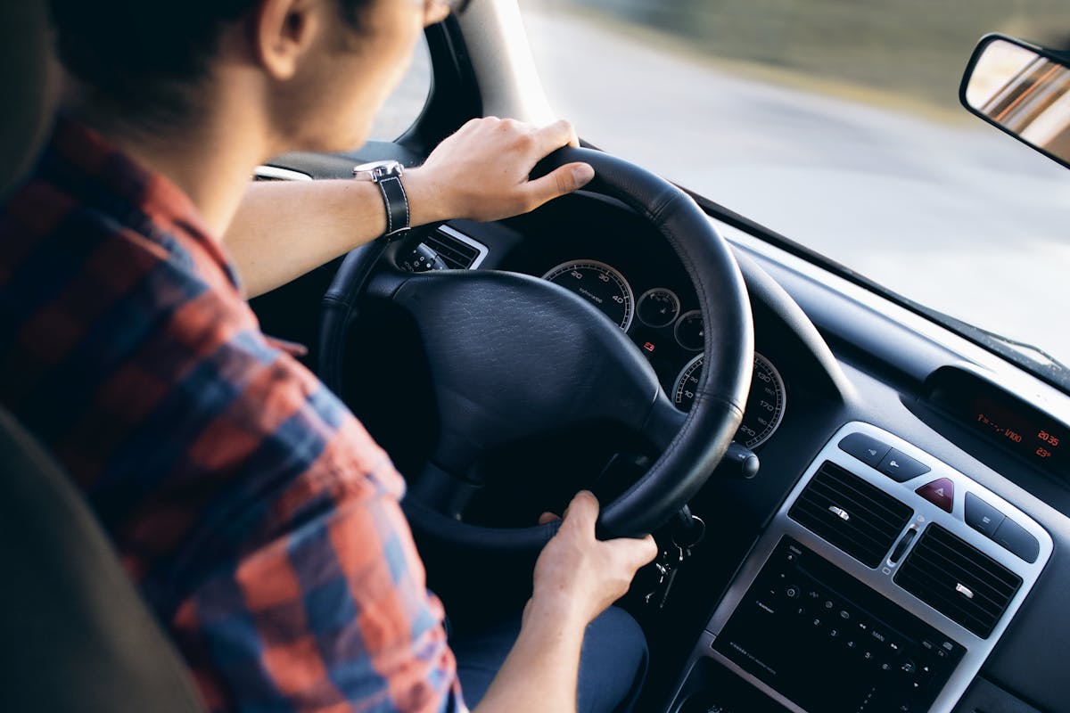 A CNH impacta na saúde mental dos novos motoristas? Close-up view of a man driving a modern car, showing dashboard and steering details.