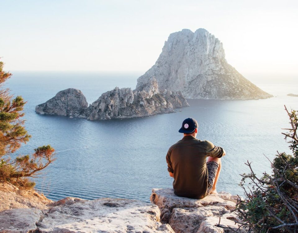 Seguro de vida e tranquilidade no dia a dia Man enjoys a scenic view of Es Vedrà at sunset from a cliff in San Juan Bautista, providing a perfect summer escape.