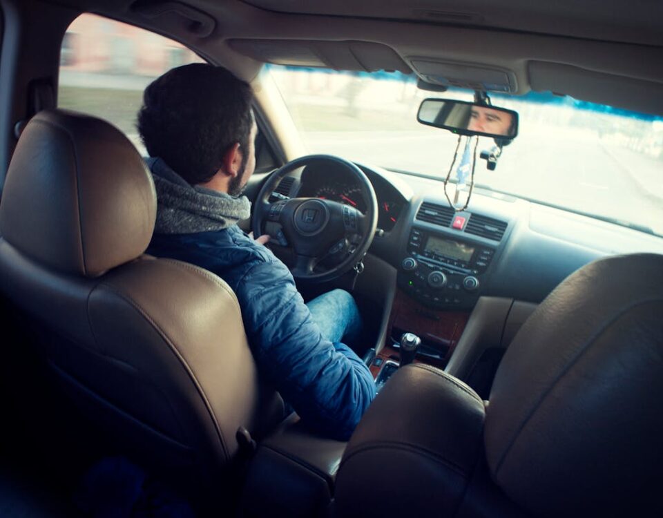 A CNH impacta na saúde mental dos novos motoristas? A man driving a car with focus on interior, dashboard, and steering wheel, captured from the backseat.
