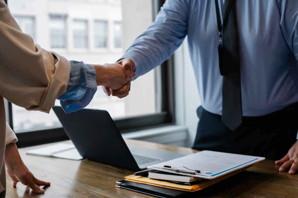 Seguro de vida e tranquilidade no dia a dia Crop unrecognizable coworkers in formal wear standing at table with laptop and documents while greeting each other before meeting