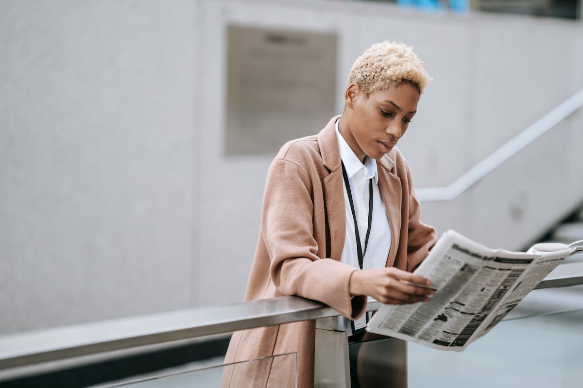 Confident businesswoman reads newspaper outdoors, conveying focus and professionalism in a modern urban environment.