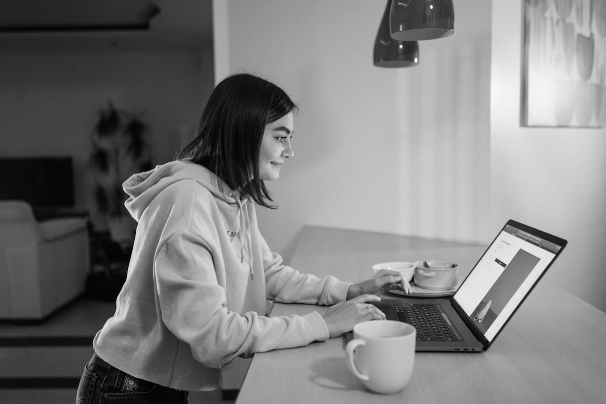 Como painéis SMM ajudam no equilíbrio entre vida e trabalho A woman sits at a table using a laptop, smiling while working indoors.
