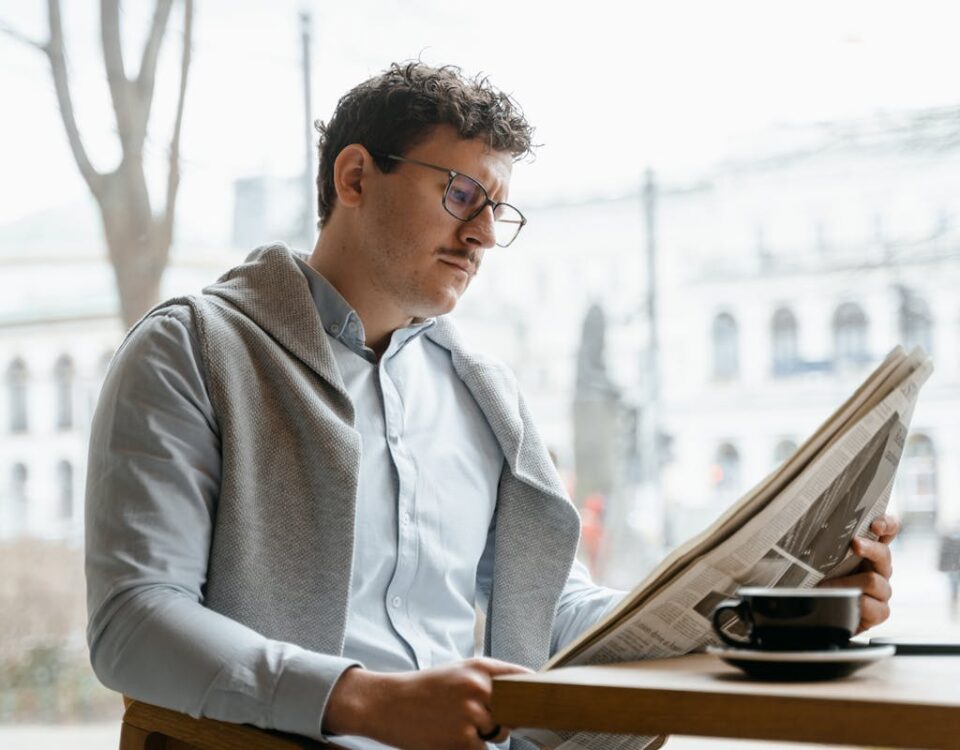 Notícias ruins afetam a saúde mental? Adult man reads a newspaper by a café window, enjoying a coffee break indoors.