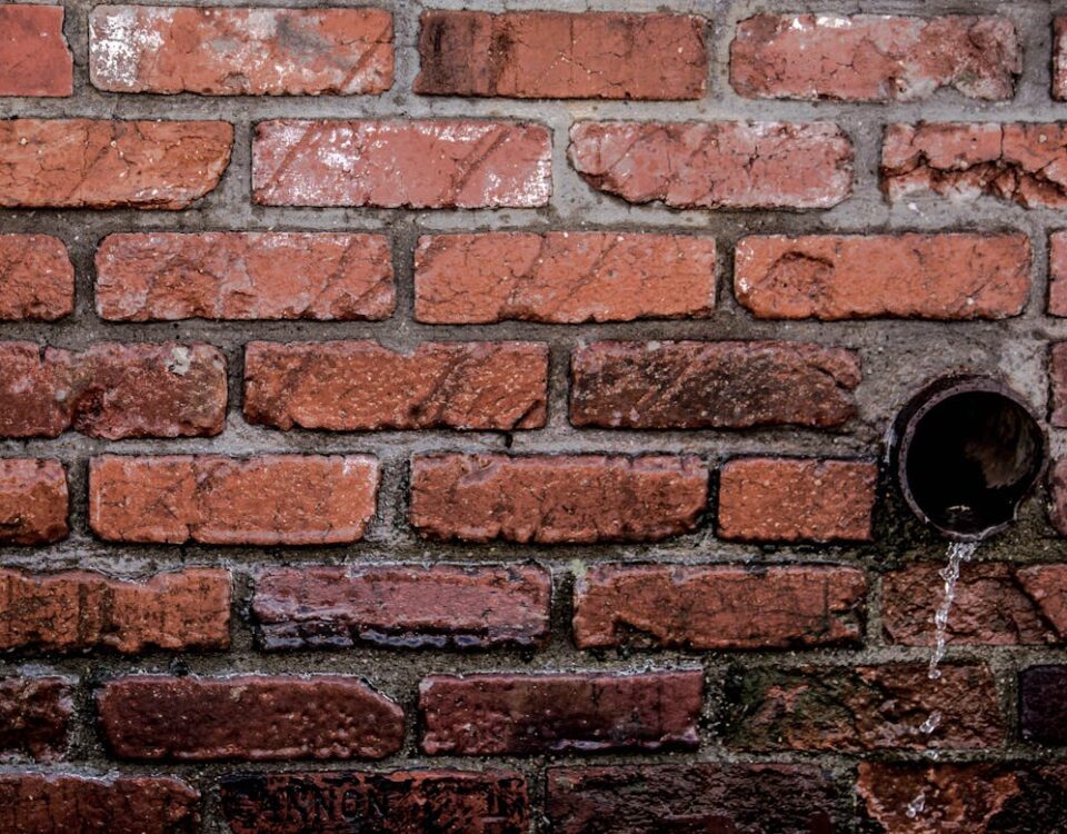 Impactos do desperdício de água no estilo de vida Close-up of a red brick wall with water flowing from a drain, showcasing texture and patterns.
