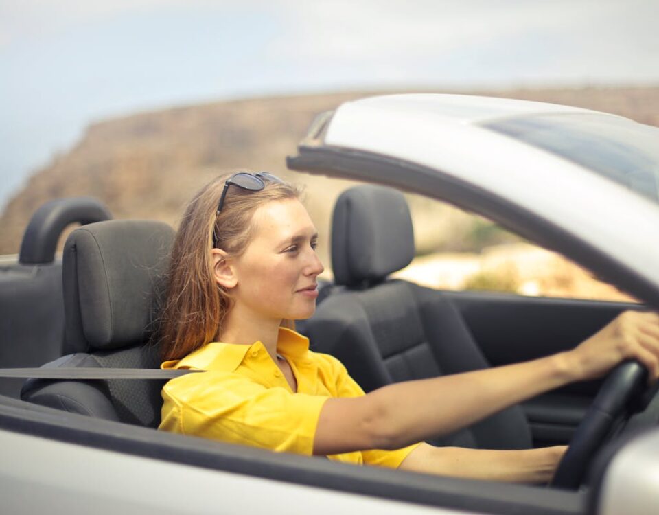 Exercícios para melhorar sua postura ao dirigir A young woman enjoys driving a convertible on a sunny day in Malta.