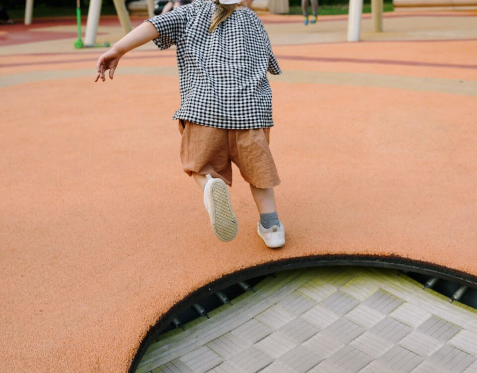 Como calçados adequados impactam a saúde das crianças A playful child jumping on a trampoline at an outdoor playground during summer.