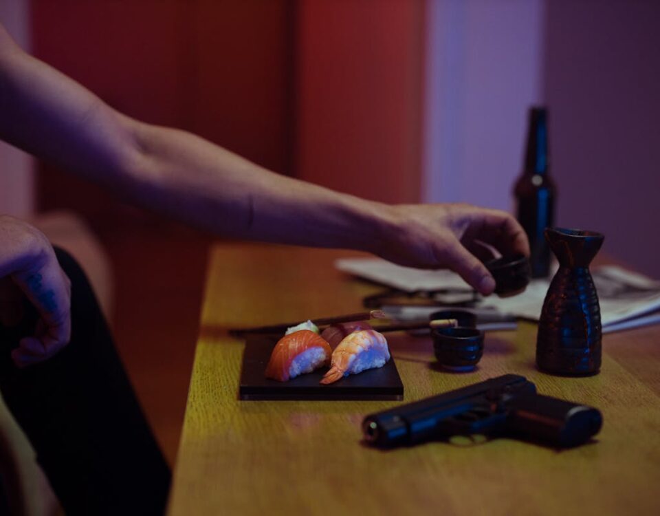 Impactos psicológicos de possuir uma arma de fogo An intriguing scene with sushi, a gun, and sake glasses on a table under warm light.