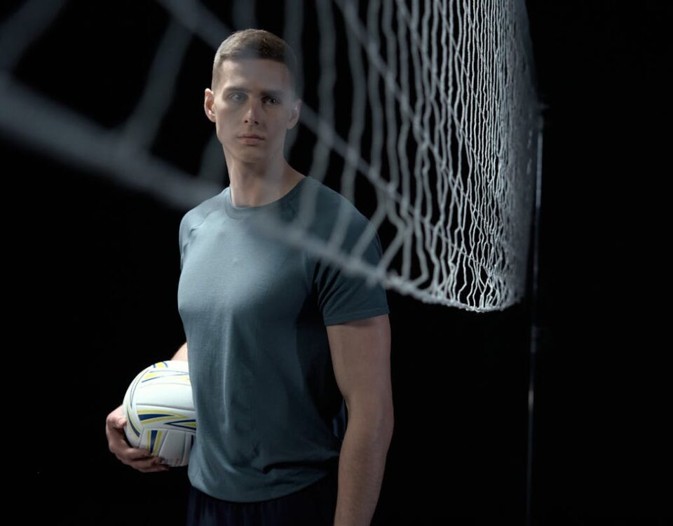 Esportes indoor: como melhorar a experiência dos clientes Athletic man holding a volleyball in a studio setting near a net.