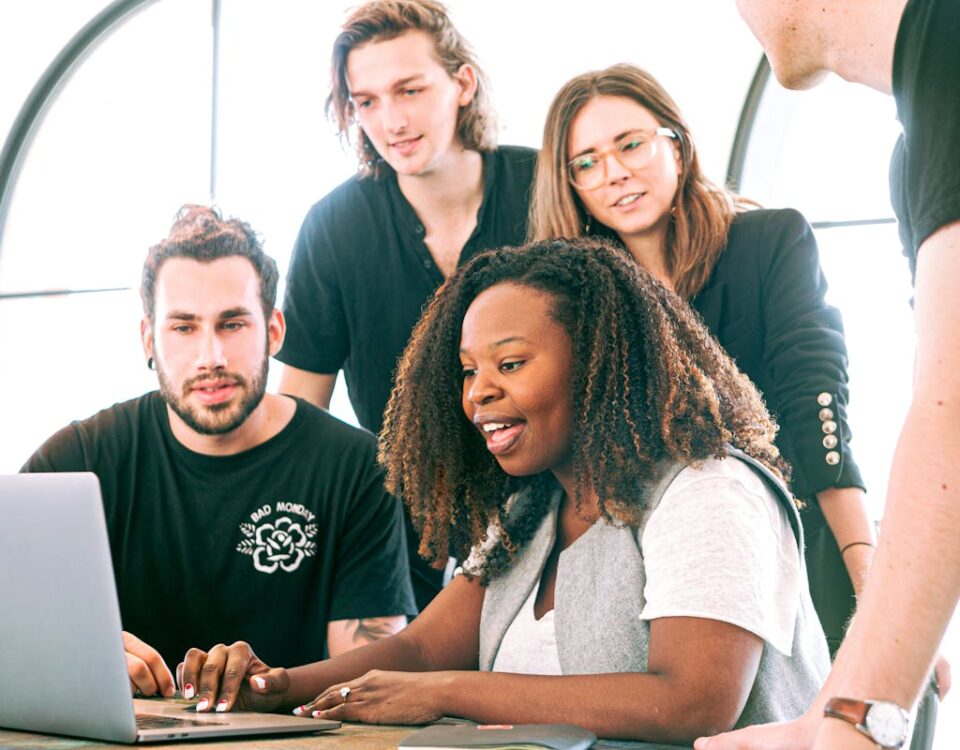 Dicas para integrar equipes internas e agências criativas A diverse group of young professionals collaborating around a laptop in a modern office setting. Perfect for business or tech concepts.