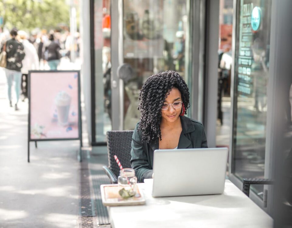 O impacto do equilíbrio emocional na liderança High angle of pensive African American female freelancer in glasses and casual clothes focusing on screen and interacting with netbook while sitting at table with glass of yummy drink on cafe terrace in sunny day