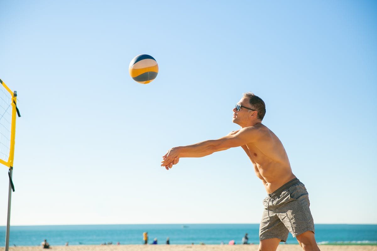 Esportes indoor: como melhorar a experiência dos clientes Shirtless man playing beach volleyball under a clear blue sky