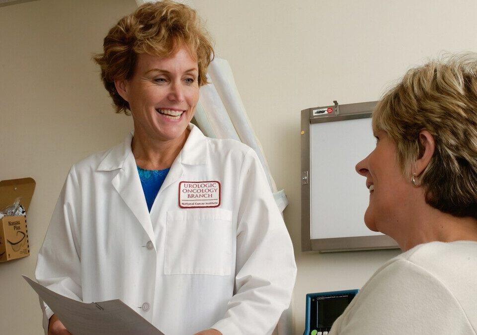 Médico de jaleco branco conversando com uma paciente em consultório