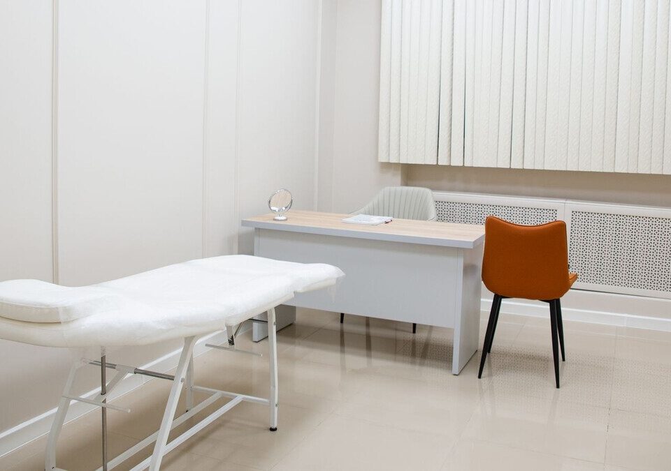 Consultório médico com mesa, cadeiras e maca