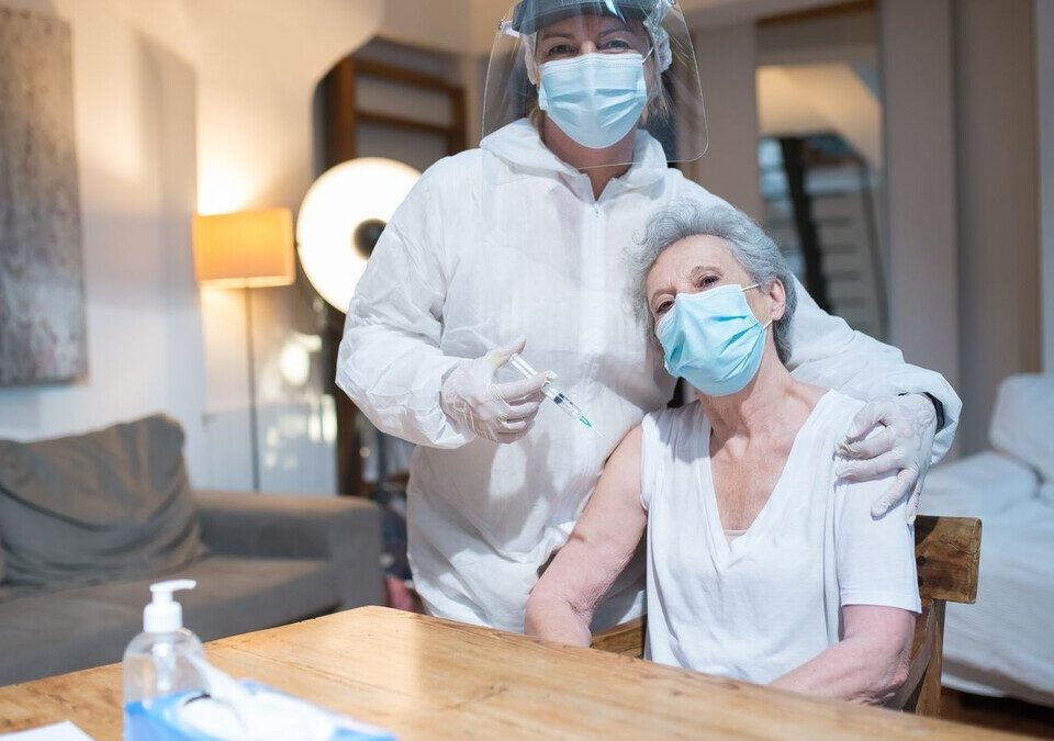 Profissional de saúde com equipamento de proteção vacina idosa em casa