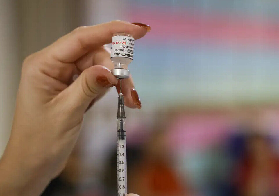 Profissional de saúde aspira dose da vacina Comirnaty de um frasco com seringa