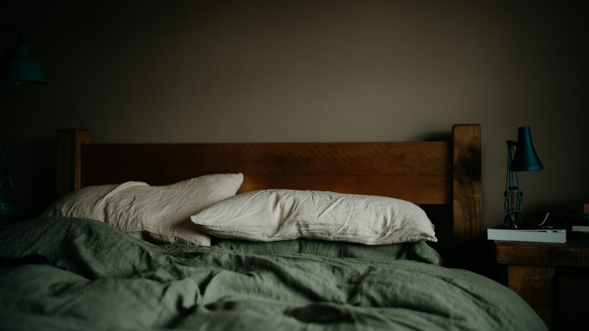 Sono e rotina para quem trabalha seis dias por semana: o que ajuda? Cama com edredom verde e abajur ao lado em um quarto