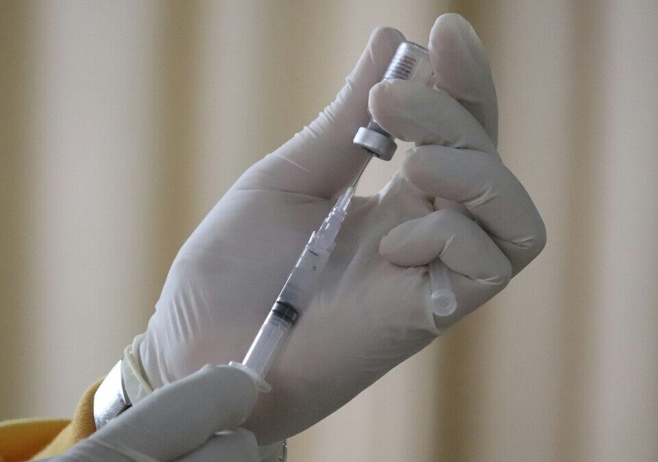 Profissional com luvas aspirando vacina de um frasco para a seringa